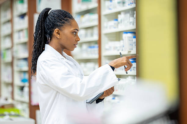 istock Pharmacist In White Lab Coat Checks Pharmacy Shelves While Holding Clipboard During Customer Service 2254176172