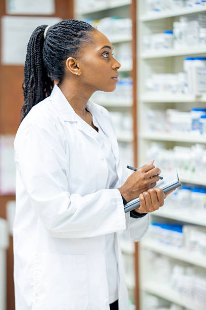 istock Black Female Pharmacist in White Lab Coat Taking Notes in a Pharmacy Setting 2254176543