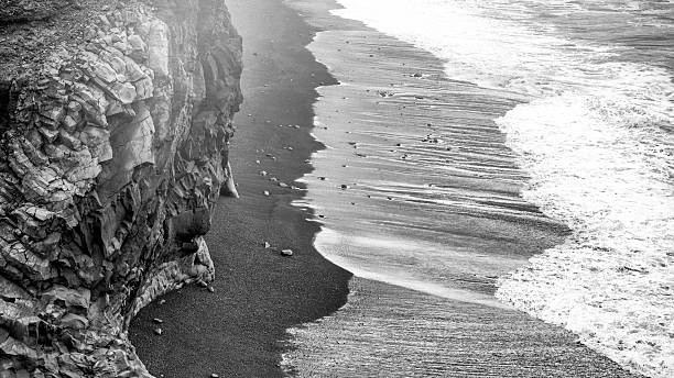Icelandic Reynisfjara beach with black sand and rocky cliffs during summer clouds.