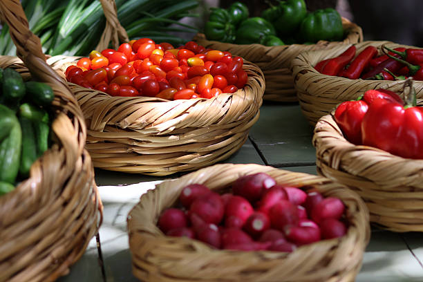 Straw baskets filled with fresh organic vegetables, ripe cherry tomatoes, red peppers, cucumbers, radishes, and green shallots.