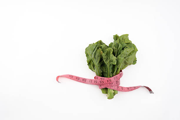 Fresh kailan vegetables wrapped with measuring tape isolated on white background representing healthy eating, diet control, nutrition awareness, and natural food choice in clean minimal presentation.