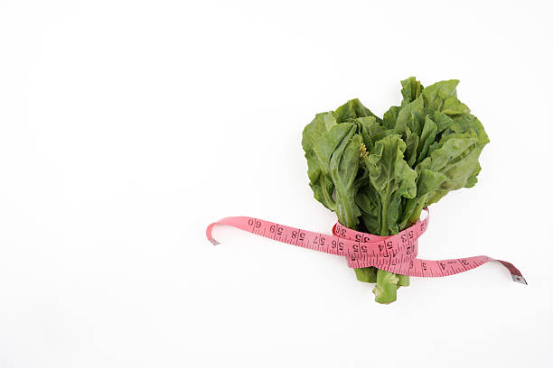 Fresh kailan vegetables wrapped with measuring tape isolated on white background representing healthy eating, diet control, nutrition awareness, and natural food choice in clean minimal presentation.