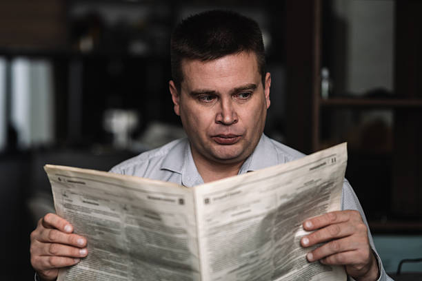 istock Smiling mature man reading newspaper while sitting at the table on dark background. 2254202414