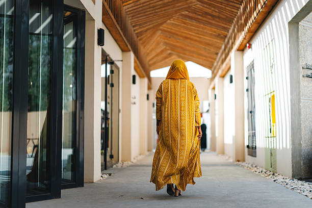 istock Middle Eastern Woman in Yellow Abaya Walking Through Modern Architectural Corridor 2254202575