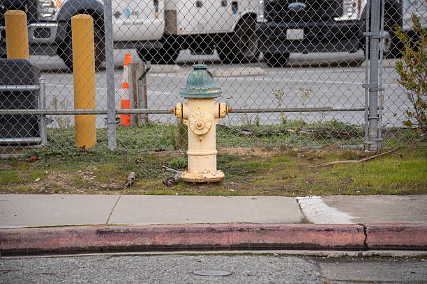 istock Yellow fire hydrant with green cap stands by a chain-link fence and road 2254213982