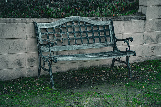 An old wooden park bench with decorative metalwork rests on a grassy area next to a weathered stone wall