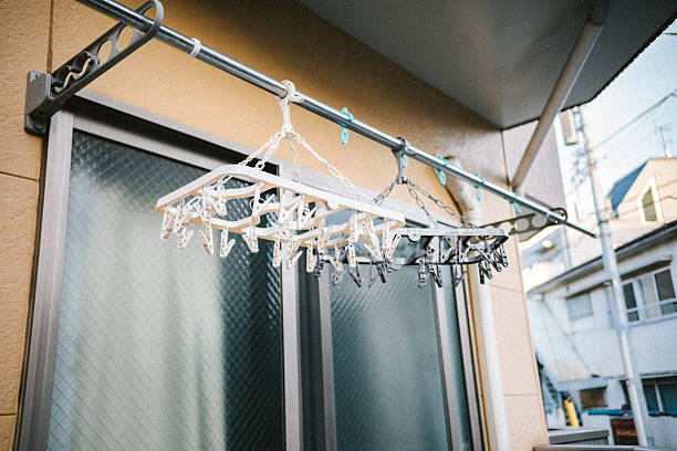 An empty clothes drying rack with neatly arranged clothespins hanging on a Japanese apartment balcony. The absence of laundry creates a quiet, contemplative scene that represents everyday life, waiting, routine, and the subtle presence of human activity.