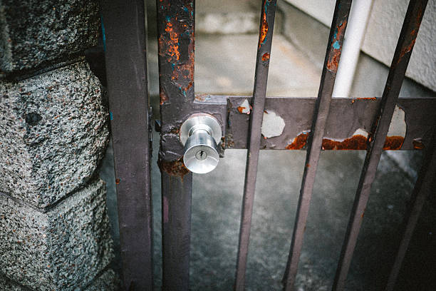 A close-up of a rusty metal gate with a locked door knob. The weathered surface and solid lock convey themes of security, restriction, boundaries, protection, and the passage of time in an urban residential setting.