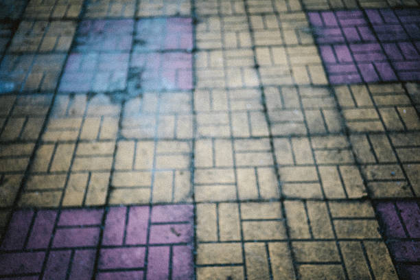 An abstract close-up of worn colorful pavement tiles. The faded yellow and purple blocks and soft focus evoke nostalgia, memory, and the passage of time, making it suitable as an urban background or conceptual texture.