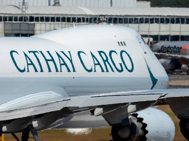 A Cathay Pacific Cargo Boeing B747-867F plane, registration B-LJB, taxiing for departure from the main runway of Sydney Kingsford Smith Airport as flight CX28 to Melbourne.  A heat haze is caused by the hot, summer weather. In the far background is a Jetstar Airbus A320-232 plane parked at the domestic terminal. This image was taken from New Link Road, Mascot on a hot and sunny afternoon on 30 December 2025.