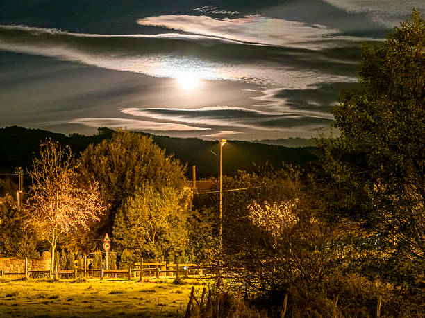 Full moon glowing behind wavy clouds, casting light on trees and a field in Basque Country