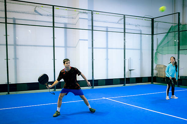 A man and woman smile while holding paddles on a bright blue indoor court, ready for a friendly match.