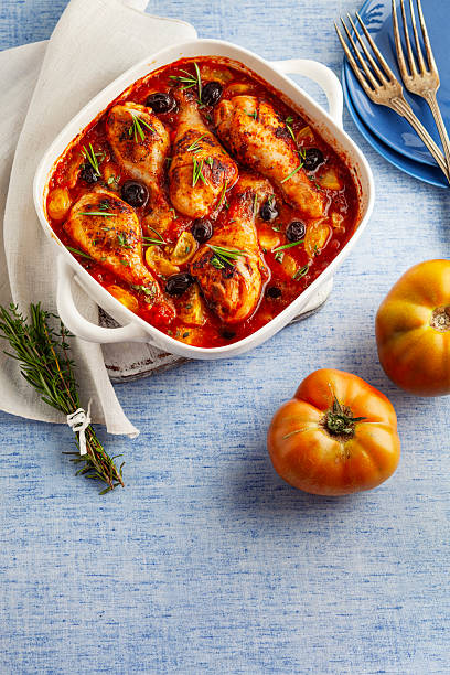 Oven-baked chicken drumsticks in tomato sauce with black olives and rosemary, rustic homemade comfort food.