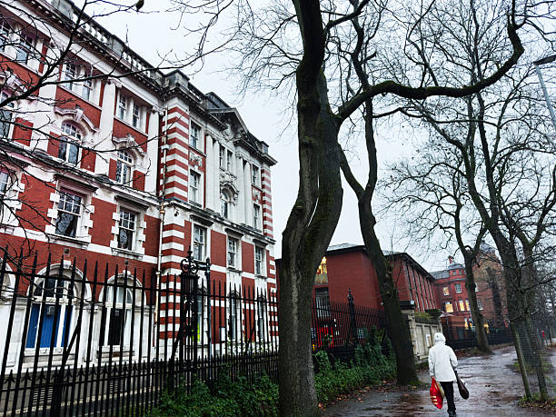 Manchester, UK - December 06, 2025: People walk past a grand striped brick building with iron fence on a wintry Manchester street.