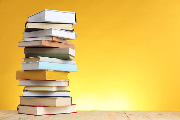 Many stacked books on table against yellow background. Space for text