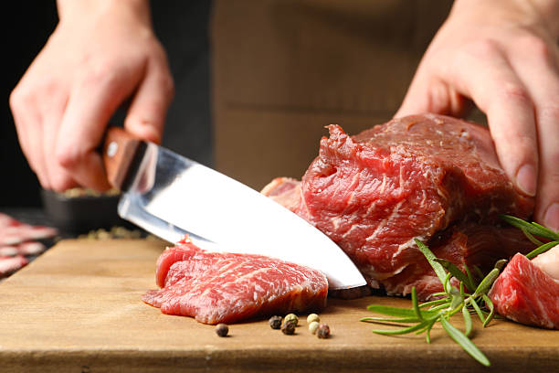 istock Woman cutting raw beef meat at table, closeup 2254243165