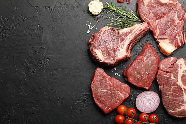 istock Pieces of raw beef meat, spices and tomatoes on black table, flat lay. Space for text 2254243182