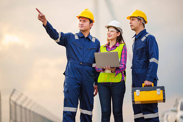 istock Renewable energy maintenance. Engineer using laptop computer checking system of wind turbine at windmill field farm station. Wind turbine energy storage system. Workers meeting to check around the area 2254246351