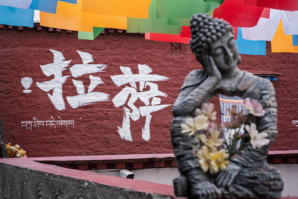 A stone-carved contemplative Buddha statue holding delicate flowers, set against a vibrant red wall with white Chinese calligraphy that reads \