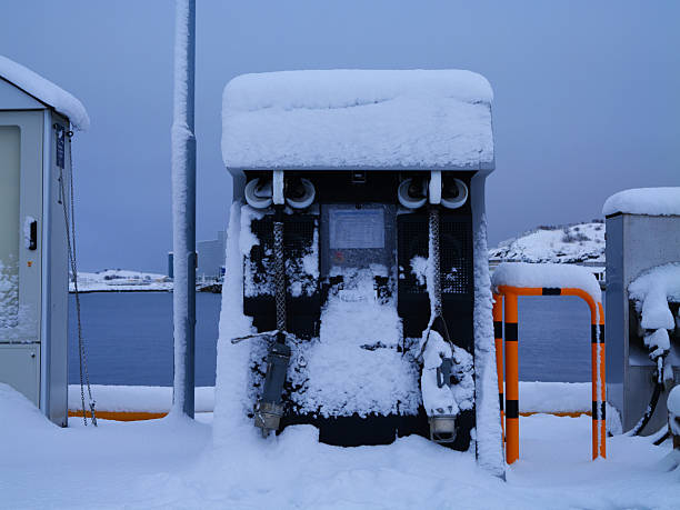 Bodo, Norway - Nov 17 2025: Snow-laden shore power hookup and charging cabinet on the quay in Bodo, Norway, under a moody winter sky by the fjord.