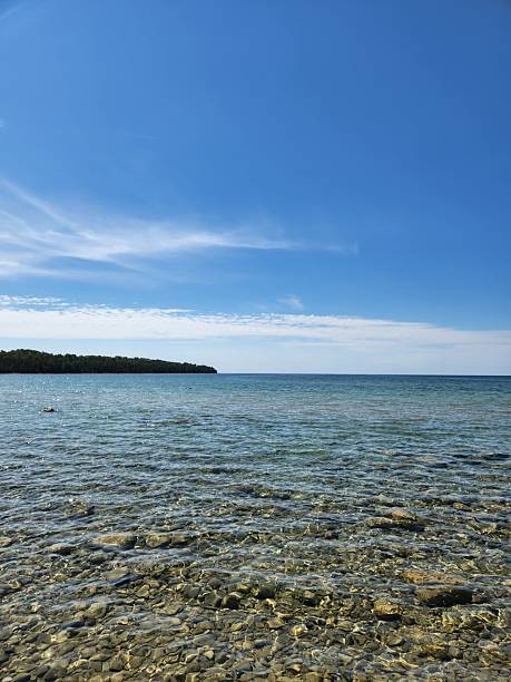 istock Rocky Lakeshore with Clear Water and Pine Trees Under Blue Sky 2254253107