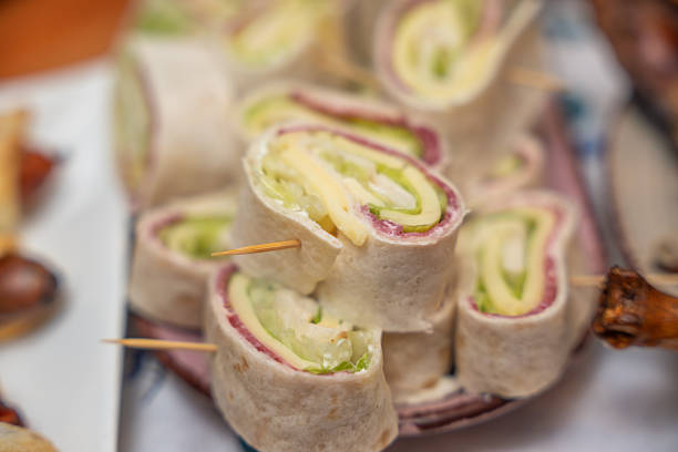 Fresh tortilla wrap rolls filled with cheese, cucumber, and cold cuts, served as bite-sized appetizers on skewers. Ideal finger food for catering, parties, and buffet events.