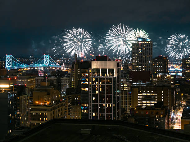 Spectacular fireworks light up the night sky over Philadelphia, showcasing the city skyline and the iconic bridge, conveying a festive atmosphere.