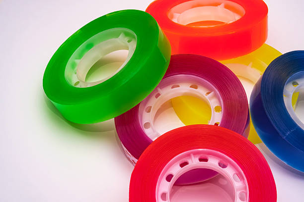 Small transparent scotch tape rolls. Vibrant close-up of multiple sellotape rolls. Bright colored adhesive sellotape scattered randomly on a clean white surface. Ideal for creative projects.
