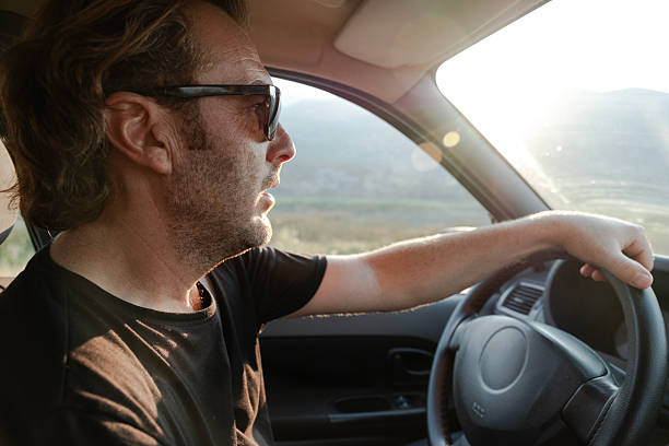 istock A man is driving comfortably, wearing sunglasses, with sunlight reflecting off the windshield. 2254262502