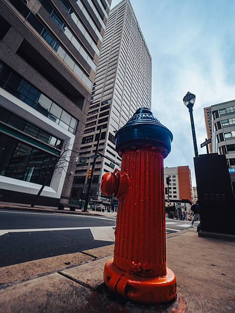 A vibrant orange fire hydrant stands prominently on a city street, showcasing urban architecture and a cloudy sky, evoking a sense of modern city life.