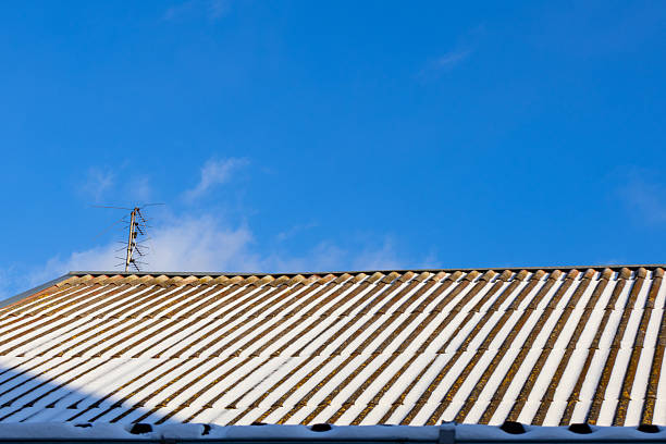 Snow blankets the roof while a clear blue sky stretches above during a bright winter day in a neighborhood setting.