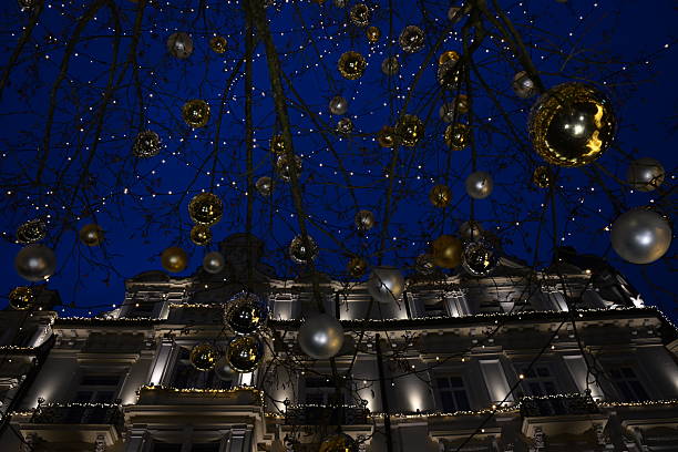Warm golden LED lights and ornaments on a tree at night. Festive holiday decorations for city streets and Christmas celebrations.
