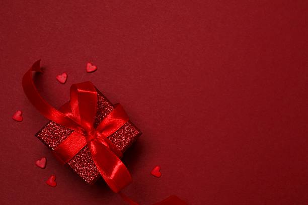 istock Festive gift box with red hearts on color background 2254276949