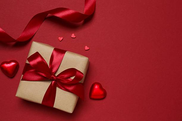 istock Festive gift box with red hearts on color background 2254276985