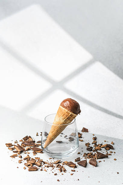 istock Waffle cone with chocolate ice cream placed in glass surrounded by scattered chocolate chunks on light surface 2254279576