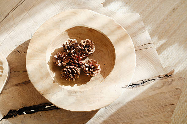 Natural pine cones rest in a wooden bowl on a textured surface with soft shadows