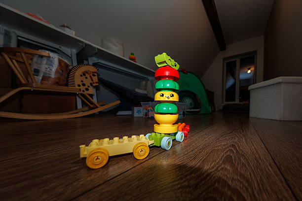 Wooden floored kids room shows a DUPLO style caterpillar train pulling a yellow trailer, a wooden rocking horse, a small tent, and toy shelves at night under flash light.