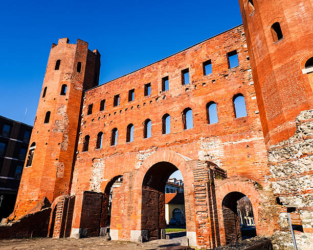 View of a historic medieval city gate in Milan, Italy, built with red brick and featuring arched entrances and defensive towers. The structure reflects the city’s rich architectural heritage and ancient urban history.