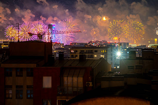December 31, 2025, Belgrade, Serbia, Colorful fireworks burst across the night sky above Belgrade rooftops cranes and city lights visible, smoke glowing as multiple explosions mark the New Year celebration over the urban skyline