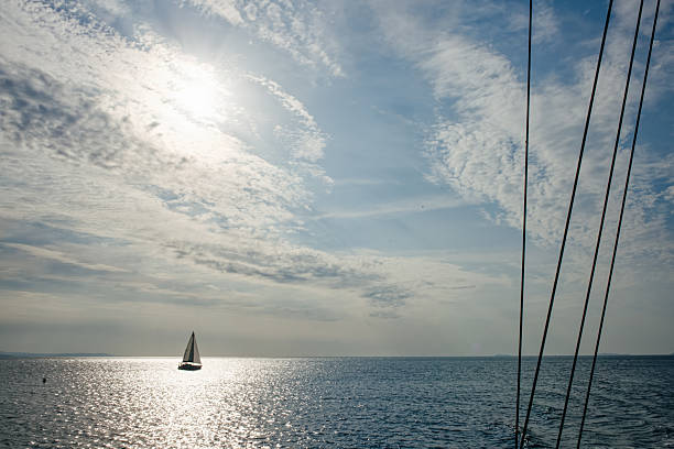 Small Sailboat Sailing on a Sparkling Sea Horizon Against a Vast Blue Sky