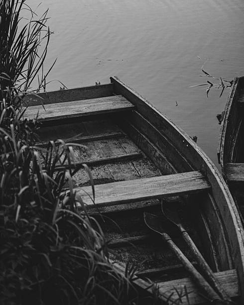 A black and white photo of an old boat resting near the riverbank. The calm water and worn texture of the boat create a nostalgic and quiet atmosphere.