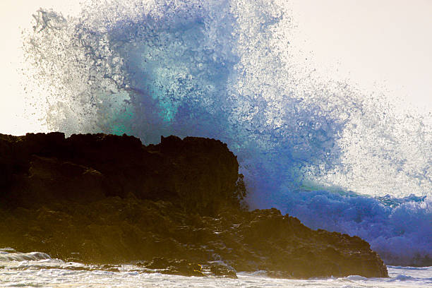 Large Ocean Wave Crashing Against Dark Rocky Shoreline