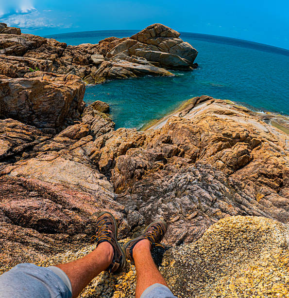 Hiker Legs Resting on Rocky Cliff Overlooking Turquoise Ocean