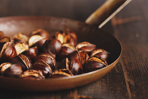 Roasted chestnuts are a delicious appetizer for wine or mulled wine for winter parties, which is easy to prepare at home. On a wooden background with fir branches
