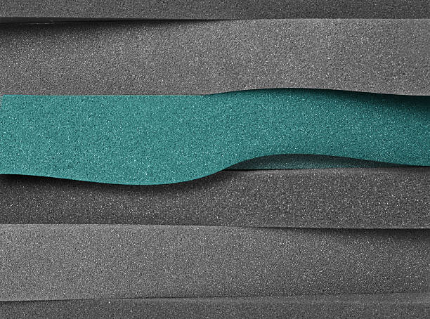 extreme close-up of a stack of thick foam sheets stacked horizontally. they are gray and green with a wavy effect.