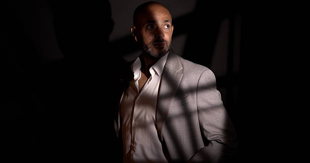 Male model wearing a suit jacket and white shirt in a studio setting, dramatic lighting creating shadows