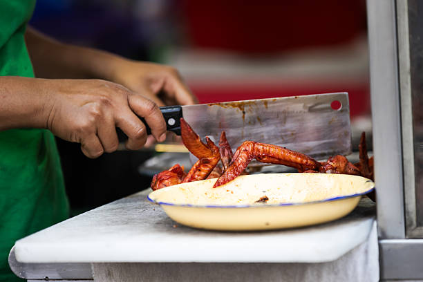 Asian street food market, Malay woman is cutting cooked chicken leg on cutting board.Penang Island - Malaysia.