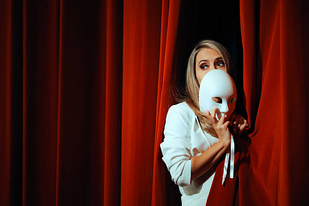 Vertical shot of senior widow wearing mourning lace veil covering womans face casting piercing glance at camera while posing seated against black background in studio under top lightning, copy space