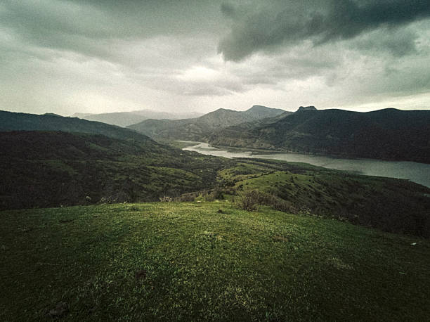 Mountain river in lush green scenic nature landscape under dark storm clouds. Biodiversity protection, sustainable resource, water conservation & environmental regeneration