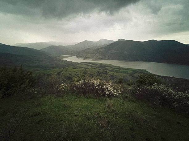 Mountain river in lush green scenic nature landscape under dark storm clouds. Biodiversity protection, sustainable resource, water conservation & environmental regeneration